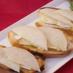 three sandwiches are on a white plate with silverware next to it and a red table cloth