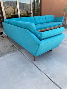 a blue couch sitting on top of a cement floor next to a window with mountains in the background