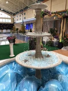 a fountain in the middle of a room filled with blue plastic bags and flowers on top of it