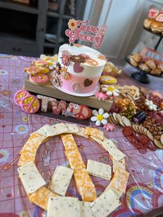 a table topped with cakes and cookies on top of a pink cloth covered tablecloth