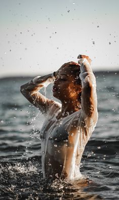 a woman standing in the water with her arms above her head