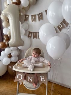 a baby sitting in a high chair with balloons around it