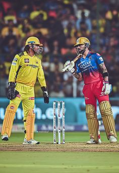 two men in yellow and red uniforms standing next to each other on a cricket field