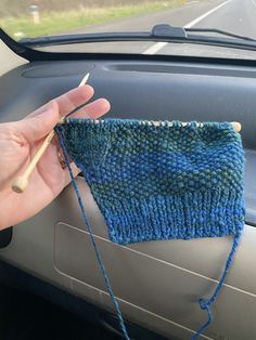 someone is knitting something on the dashboard of a car with their hand in front of them