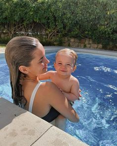 a woman holding a baby in her arms next to a swimming pool with blue water