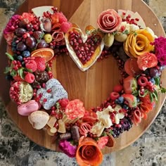 a heart shaped cake decorated with fruit and flowers on a wooden platter in the shape of a heart