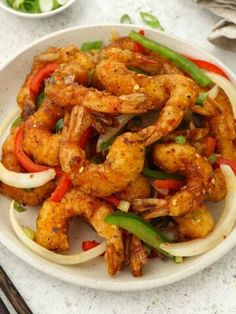 a white plate topped with shrimp and vegetables next to chopsticks on a table