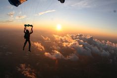 a person is parasailing over the clouds at sunset