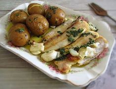 a white plate topped with meat and potatoes on top of a wooden table next to utensils