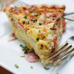 a slice of quiche with ham and cheese on a white plate next to a fork