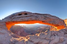 an arch shaped rock formation with the sun shining through it's opening in the distance