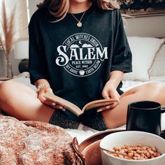 a woman is sitting on the bed reading a book and drinking coffee while eating cereal