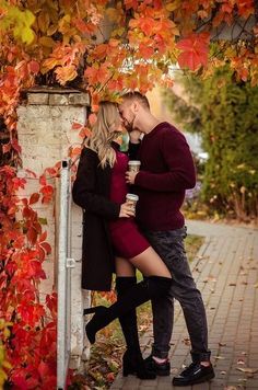 a man and woman kissing under an umbrella in front of some trees with red leaves