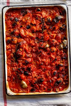 a casserole dish with tomatoes and olives in it on a table cloth