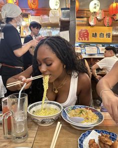 a woman eating noodles with chopsticks at a restaurant