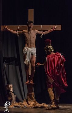 a man standing on top of a wooden cross next to a person wearing a red cape