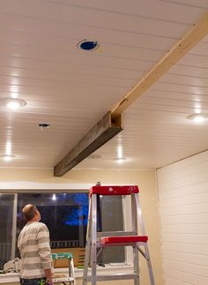 a man standing on a step ladder in front of a kitchen with wood beams attached to the ceiling