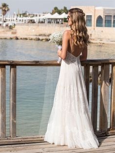 a woman in a wedding dress is standing on a pier looking out at the water