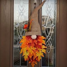 a scarecrow's hat hanging on the front door with autumn leaves around it