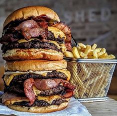 three hamburgers stacked on top of each other next to a basket of french fries