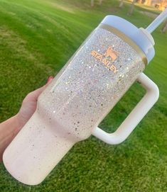 a person holding up a white and blue glittered drink in their left hand on the grass