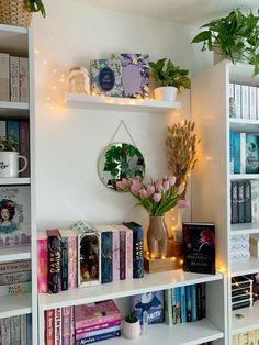 a white book shelf filled with lots of books next to a vase full of flowers