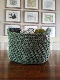 a green crocheted basket sitting on top of a wooden table next to pictures