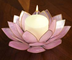 a lit candle sitting on top of a purple flower shaped object with leaves around it