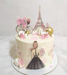 a white cake with pink and gold decorations on it's side, featuring a woman in front of the eiffel tower