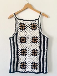 a black and white crocheted top hanging up on a hanger next to a wall