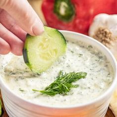 someone dipping a cucumber into a bowl of dip