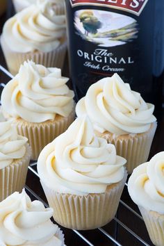 cupcakes with white frosting sitting on a cooling rack next to a bottle of beer