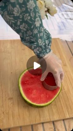 a person cutting up a piece of watermelon on top of a wooden table