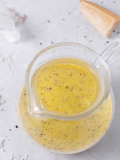 a glass jar filled with yellow liquid next to bread on a white counter top and two slices of bread in the background