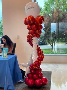 a woman sitting at a table in front of a balloon column with red and white balloons