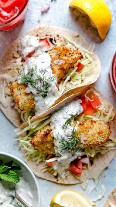 two fish tacos with sour cream sauce and garnished with lemon wedges