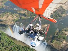 two people are parasailing over a waterfall with rainbows in the sky behind them