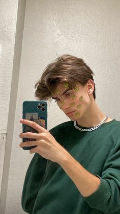 a young man with his face painted green and holding a cell phone in front of him