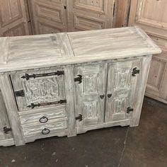 an old white wooden cabinet with doors and drawers on the bottom, in front of other antique wood cabinets