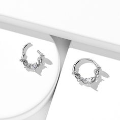 a pair of diamond hoop earrings sitting on top of a white table next to a card