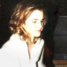 a woman with long hair wearing a white shirt and looking at her cell phone in the dark