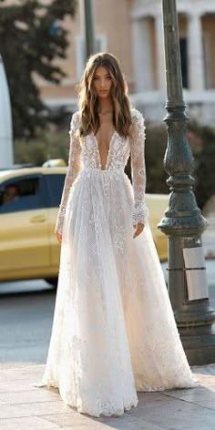 a woman is walking down the street wearing a wedding dress with long sleeves and an open back