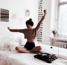 a woman sitting on top of a bed with her arms in the air while holding an old record player