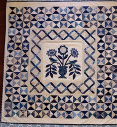 a blue and white quilt with flowers in the center on a wooden tablecloth background