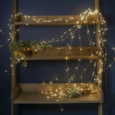 a wooden shelf filled with christmas lights and greenery next to a blue painted wall