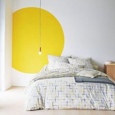 a bed sitting in a bedroom next to a yellow and white painting on the wall