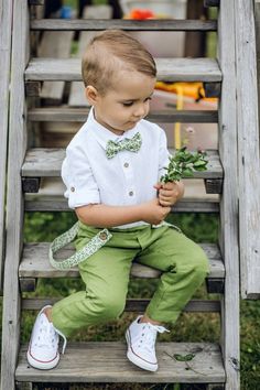 a little boy sitting on some steps with flowers in his hand and wearing a bow tie