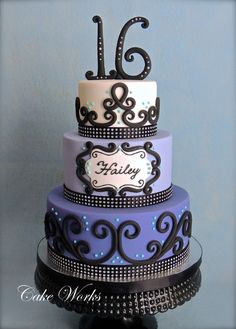 a three tiered cake is decorated with black and white icing, blue and purple fondant