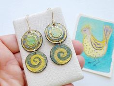 Unique funky artisan handpainted watercolor paper earrings on handmade gold filled earwires and a special original watercolor bird painting. The top component has a few layers of circles glued together with hand painted detal and gilded with gold paint. The lower circle has a wave design in a teal blue and gold. The reverse side of both pieces have printed paper that I glued on. I sanded the edges and sealed them and the entire piece with acrylic sealer and gave them a painted edge. See all 10 p Watercolor Jewelry, Shrinky Dink Earrings, 60s Jewelry, Recycled Earrings, Period Pieces, Dopamine Dressing, Blue Green Gold, Paper Earrings, Paper Jewelry