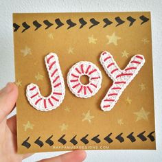 a hand holding up a card with the word joy spelled out in red and white yarn